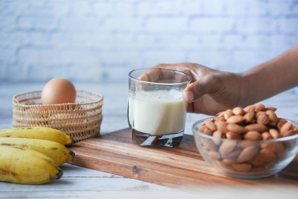 Vaso de leche, huevo y un bol de almendras sobre una tabla de madera, ejemplos de alérgenos alimentarios