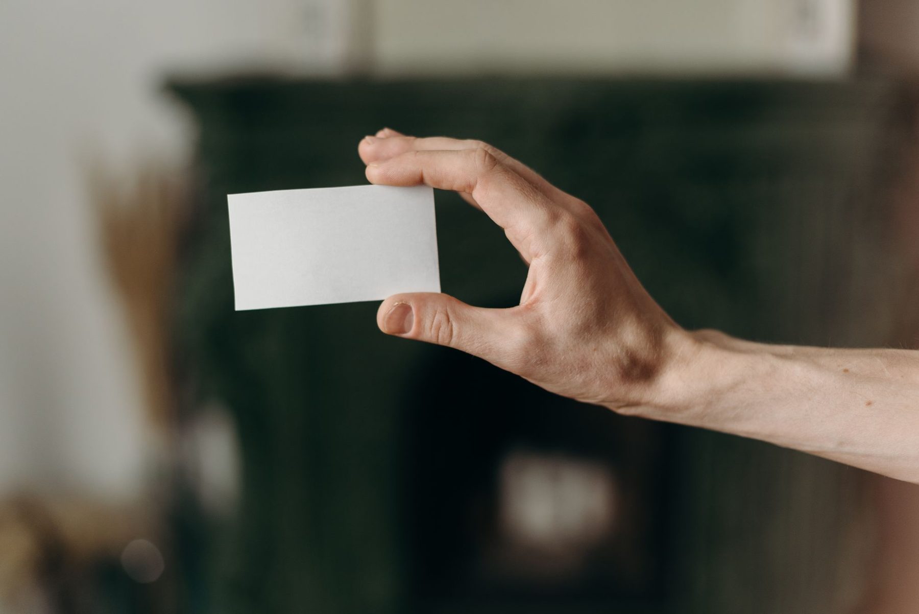 Mano sosteniendo un carnet o tarjeta en blanco, sin datos ni logotipos, sobre un fondo desenfocado