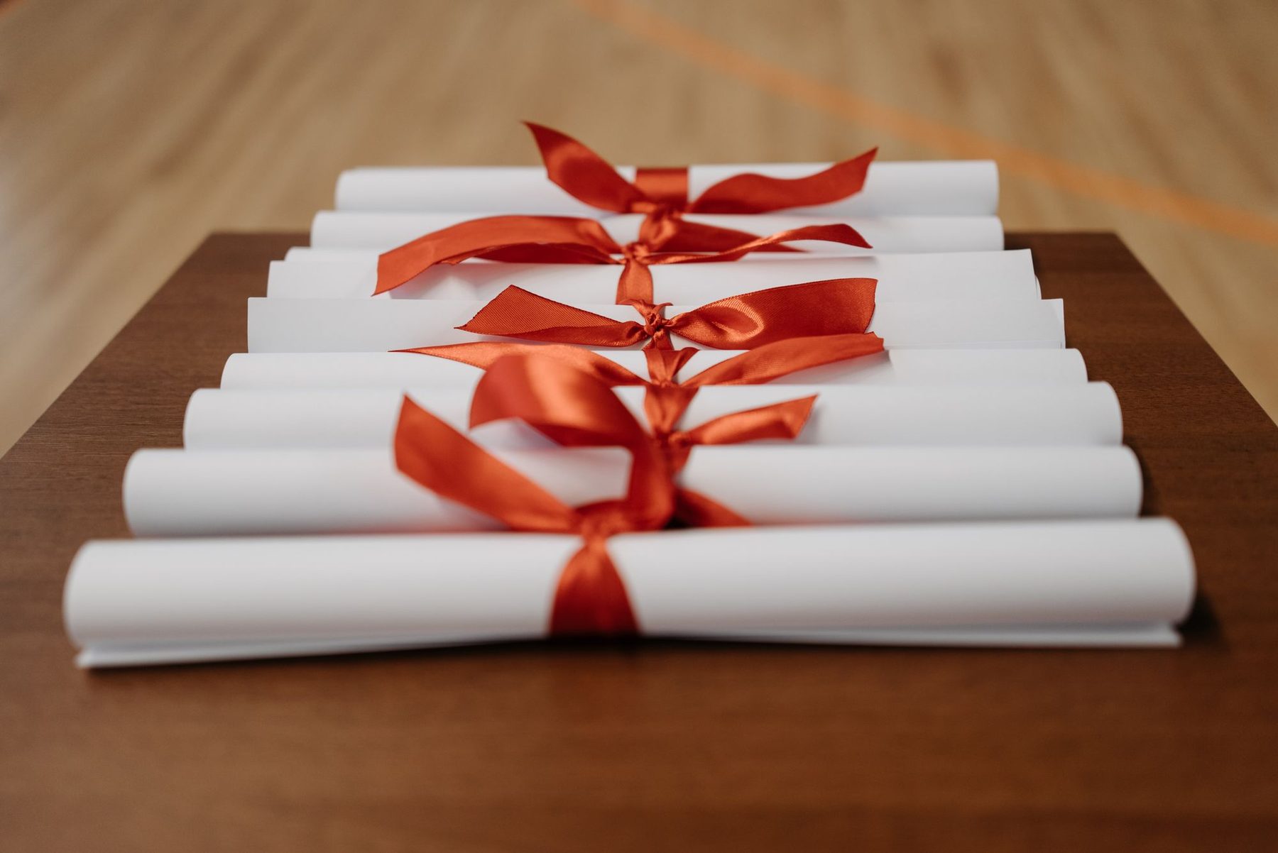 Certificados en papel enrollados y atados con lazo rojo, alineados sobre una mesa de madera
