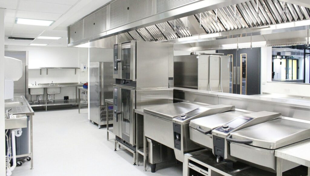 Cocina profesional vacía y muy limpia con campana extractora, hornos y mesas de acero inoxidable