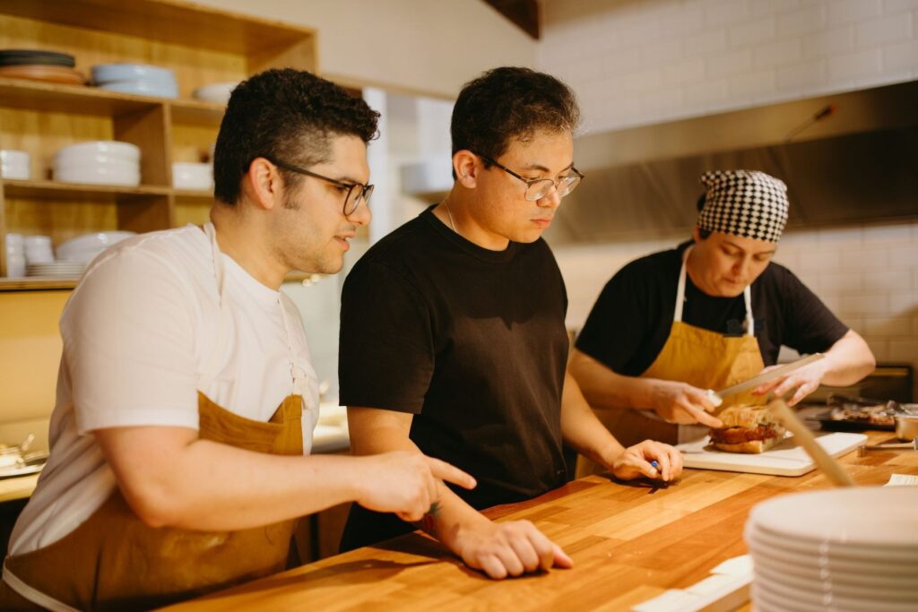 Tres cocineros de distintos orígenes trabajando juntos y coordinándose en la encimera de una cocina de restaurante