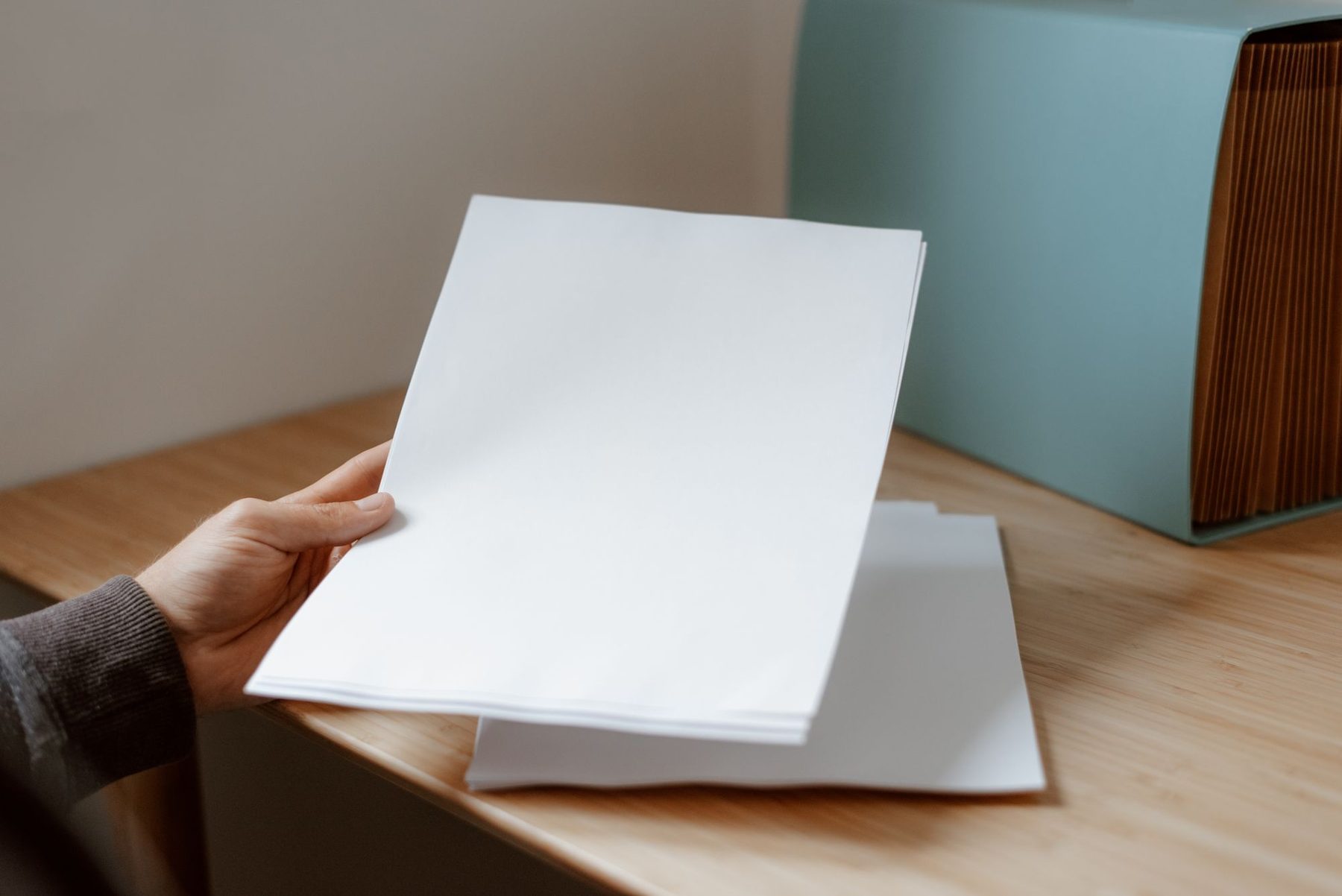 Mano sosteniendo dos hojas de papel sobre una mesa de madera junto a una carpeta archivadora