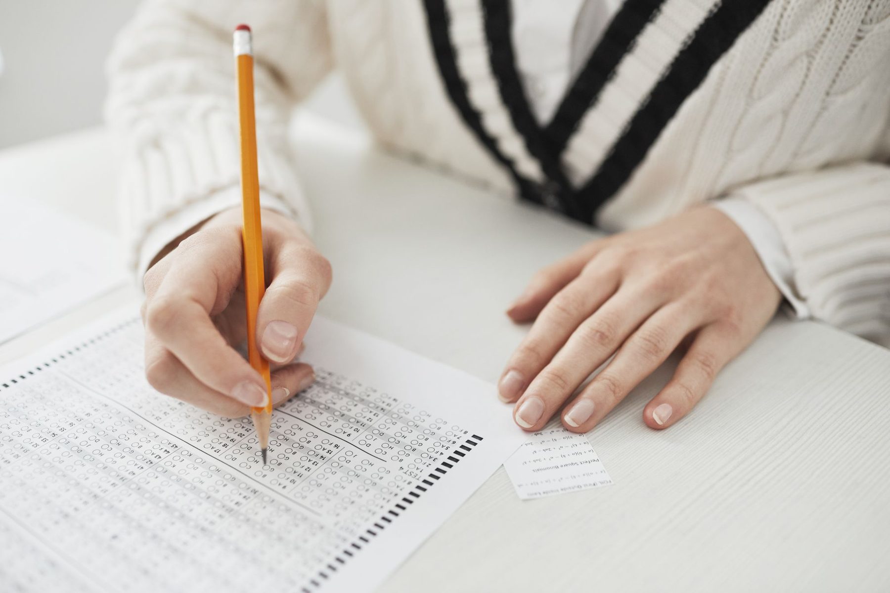 Manos de una persona rellenando con lápiz una hoja de examen tipo test sobre una mesa blanca