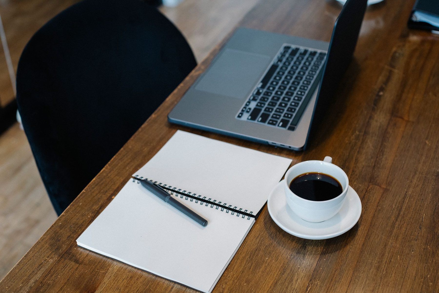 Mesa de madera con portátil, cuaderno de espiral con bolígrafo y una taza de café para estudiar