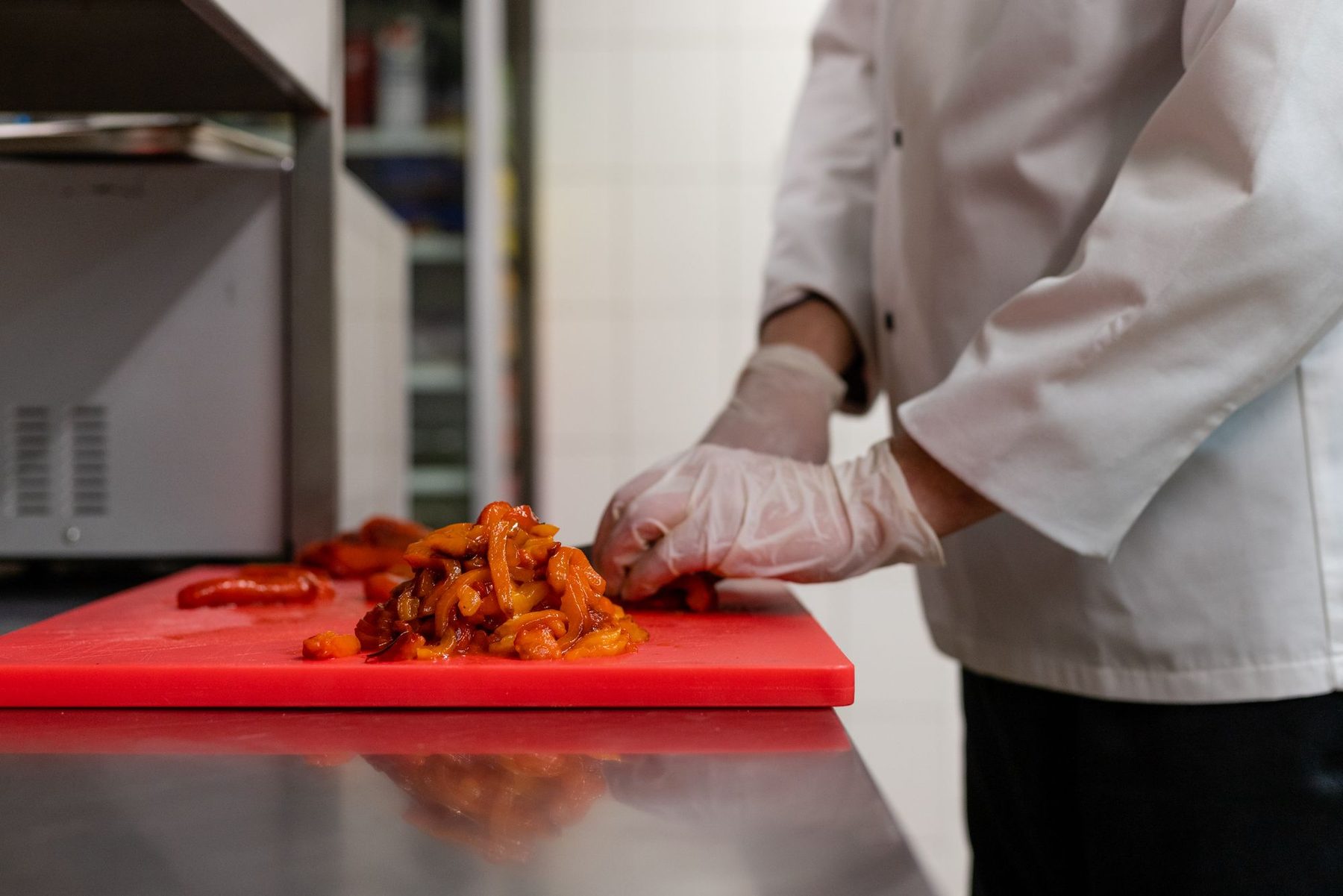 Cocinero con guantes desechables cortando verdura sobre una tabla roja en una cocina profesional limpia