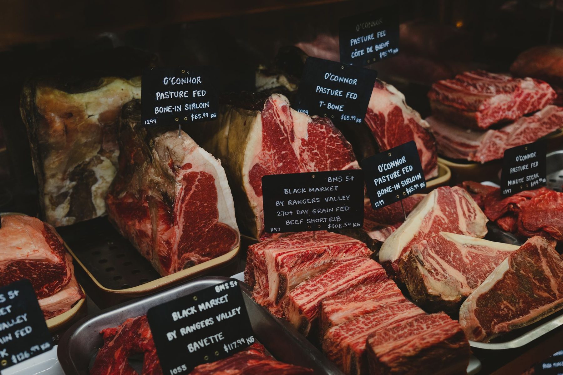 Mostrador de carnicería con cortes de carne en bandejas y etiquetas de origen y precio