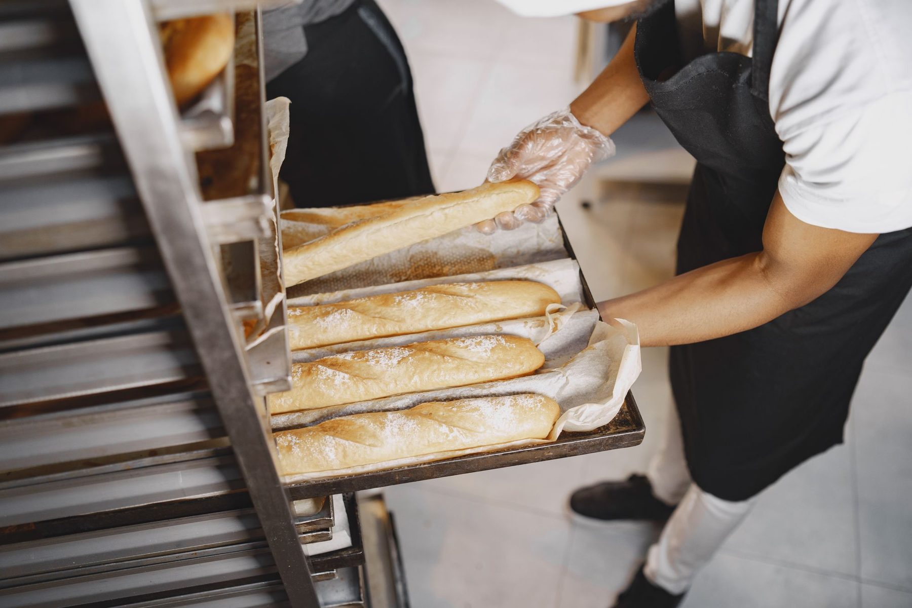 Panadera con guantes desechables colocando barras de pan recién horneadas en una bandeja