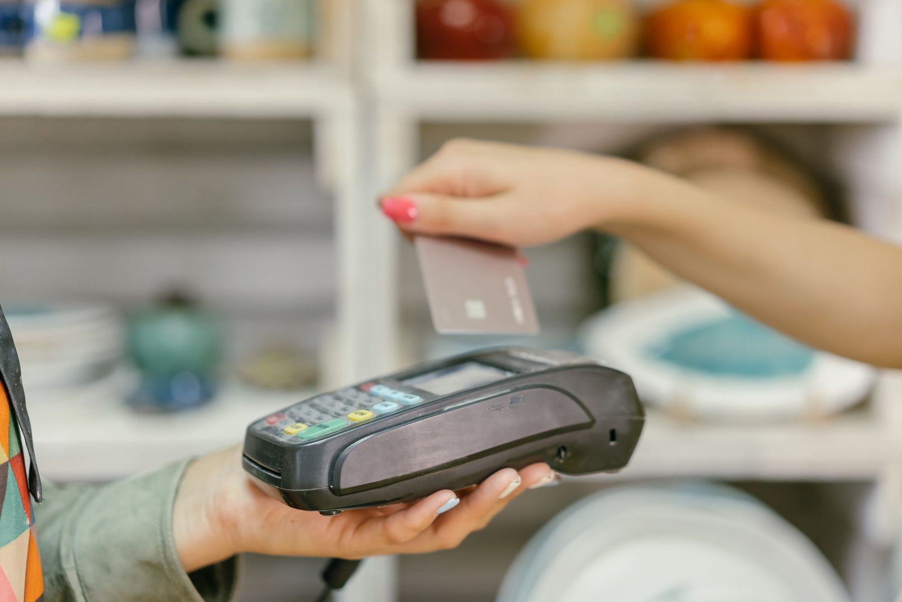 Pago con tarjeta acercada a un datáfono en el mostrador de un pequeño comercio