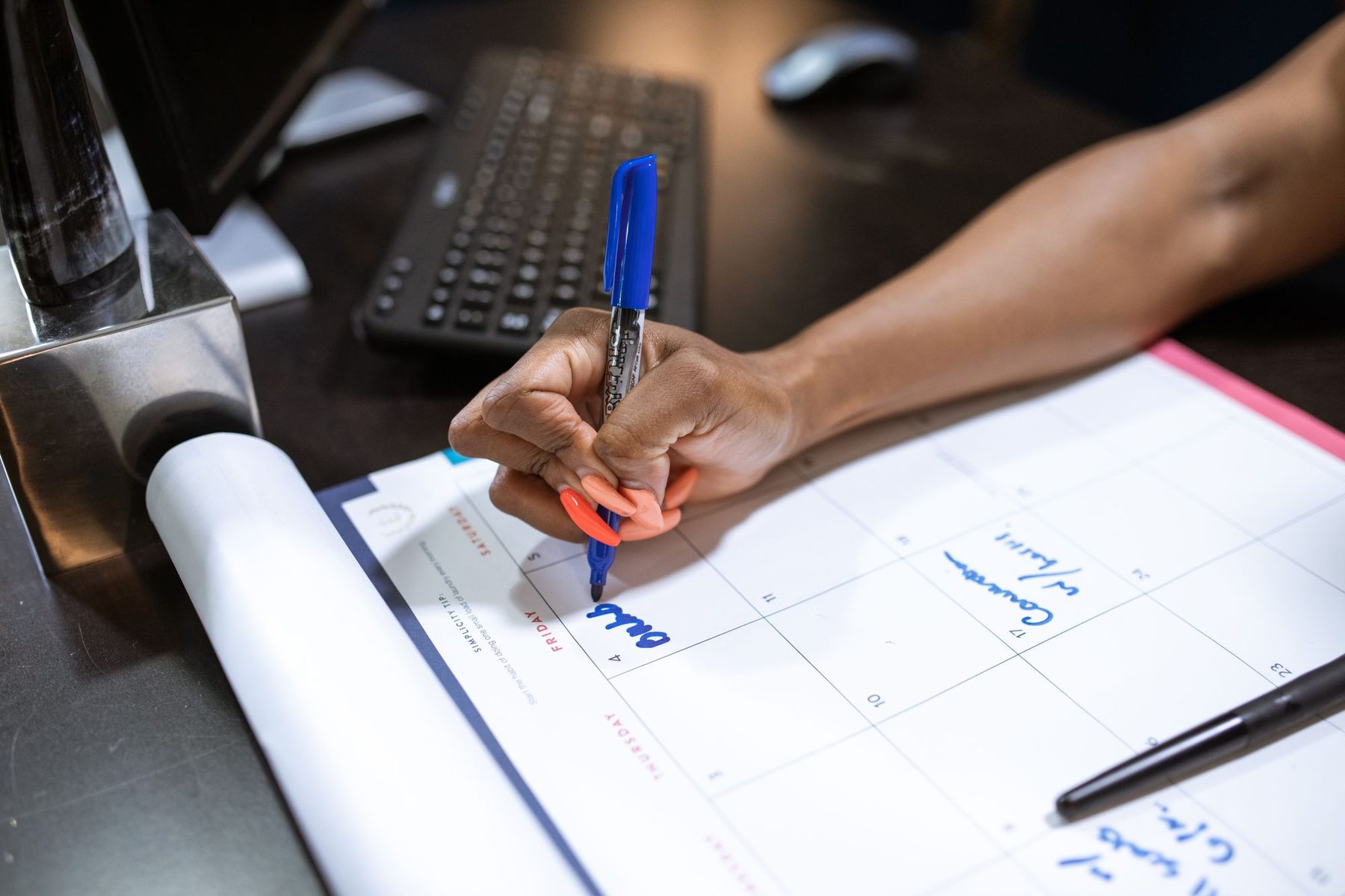 Mano marcando una fecha con un rotulador azul en un calendario mensual de mesa
