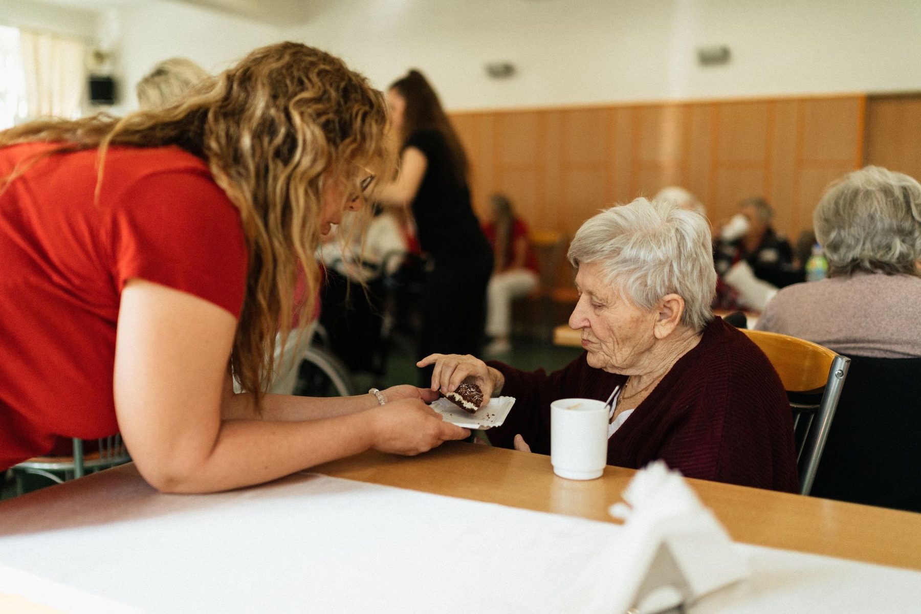 Cuidadora atendiendo a una persona mayor durante la comida en el comedor de una residencia