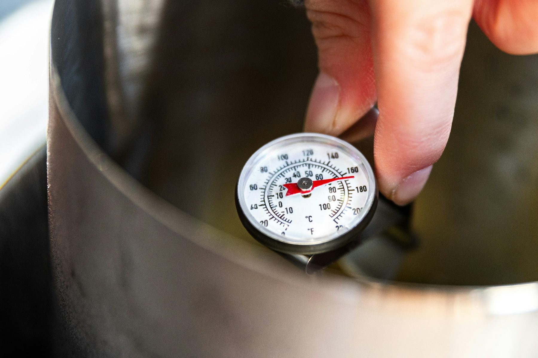 Mano sosteniendo un termómetro analógico de cocina dentro de una olla para controlar la temperatura del alimento